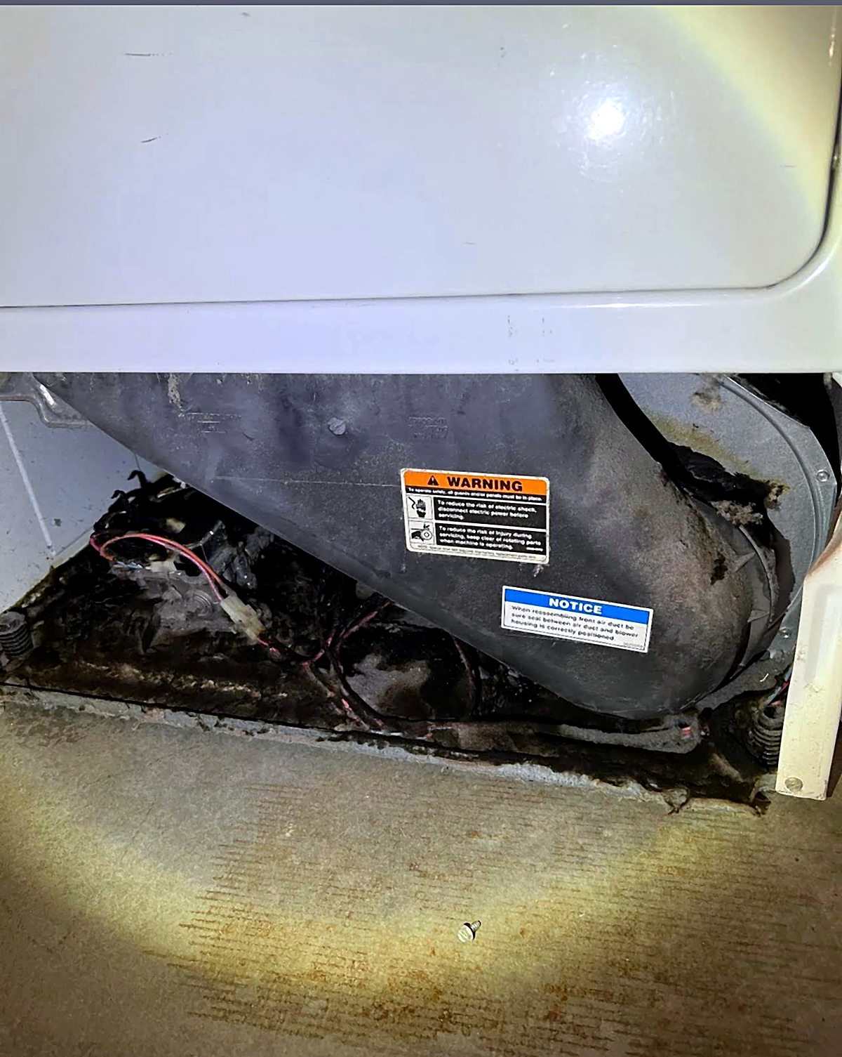 Inside a dryer with the front panel removed: the air duct housing, warning labels, and heat damage at the base of the cabinet